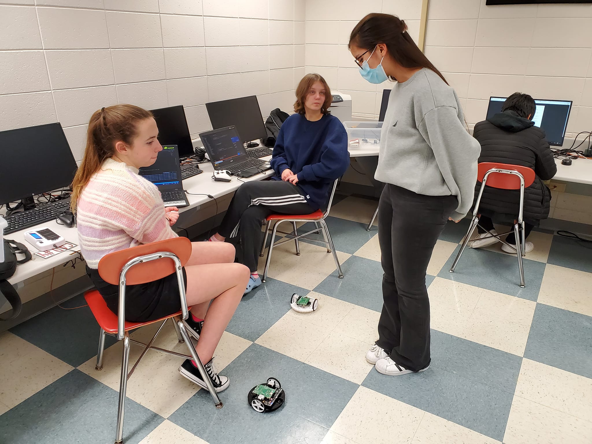Programmers Brooke Bazeley, Zoe Olson, and Jazmin Cederberg work with mini Romi robots to learn about the code base for the big robot